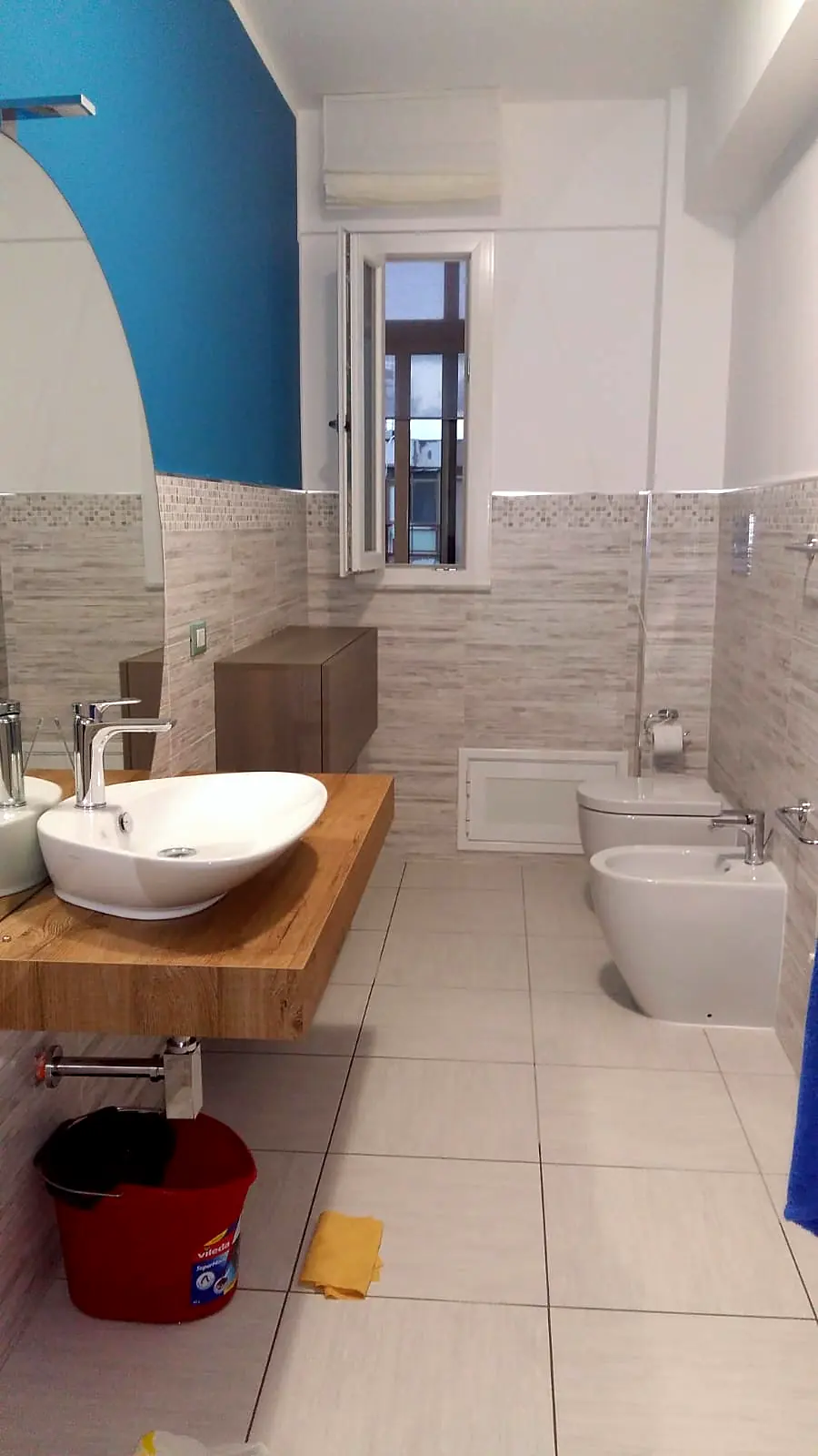 Bagno con parete azzurra, lavabo d’appoggio su mensola in legno e sanitari