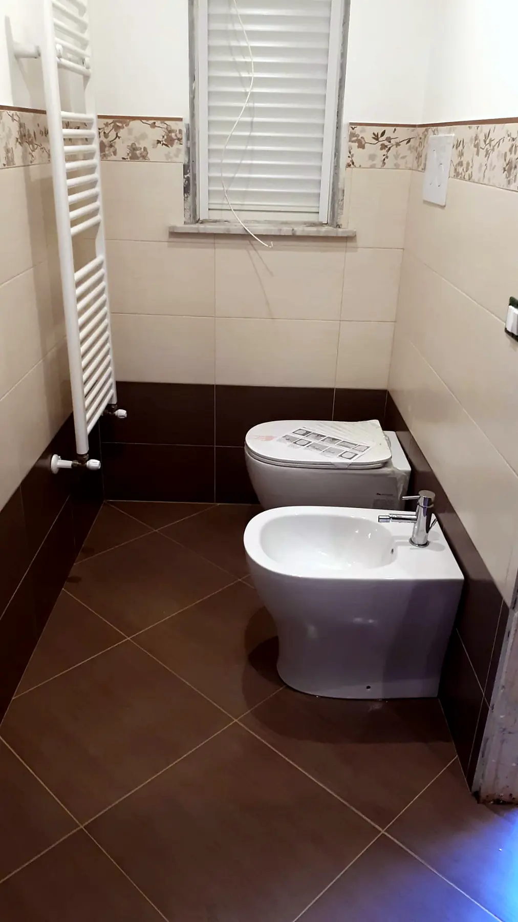 Bagno con rivestimento bianco, fascia decorata e sanitari
