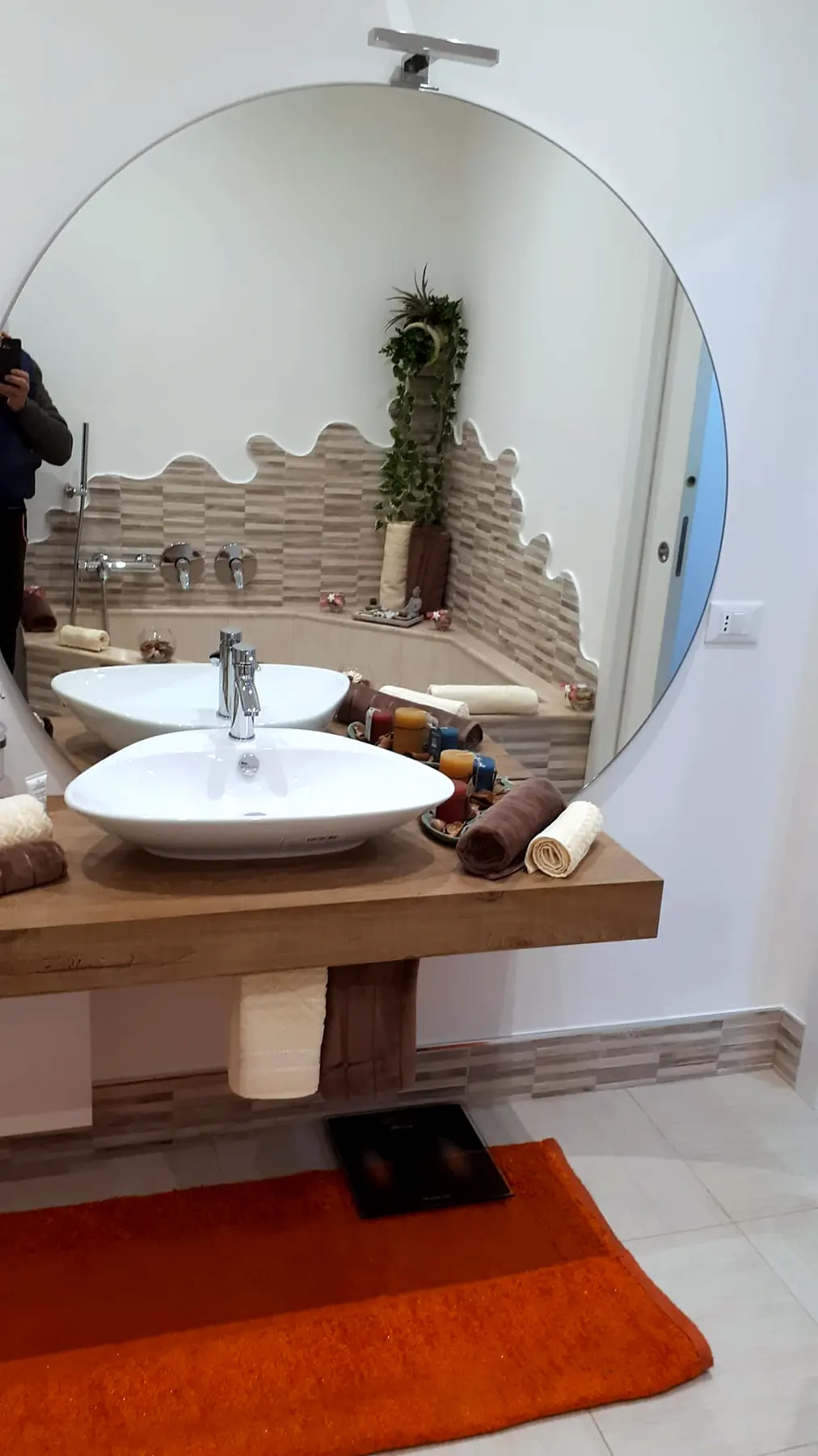 Bagno ristrutturato con due lavabi d’appoggio su mensola in legno e specchio tondo