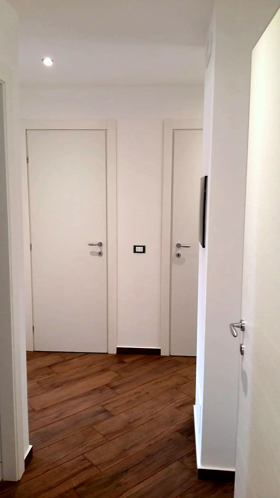 Corridoio con porte bianche e pavimento effetto legno dopo la ristrutturazione