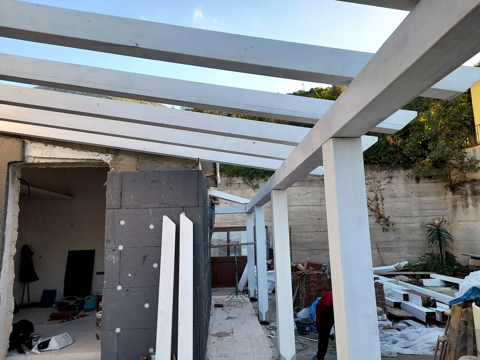 Pilastri e travi di un porticato in legno bianco davanti a una villa in costruzione
