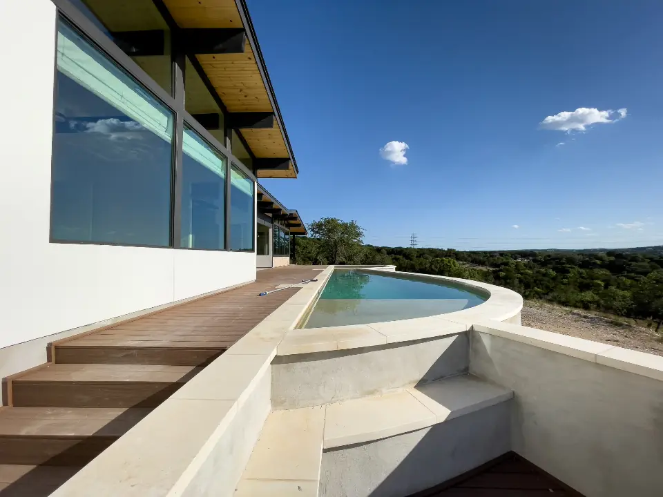 Piscina a sfioro appena realizzata accanto a una casa moderna, con bordo in pietra e deck in legno