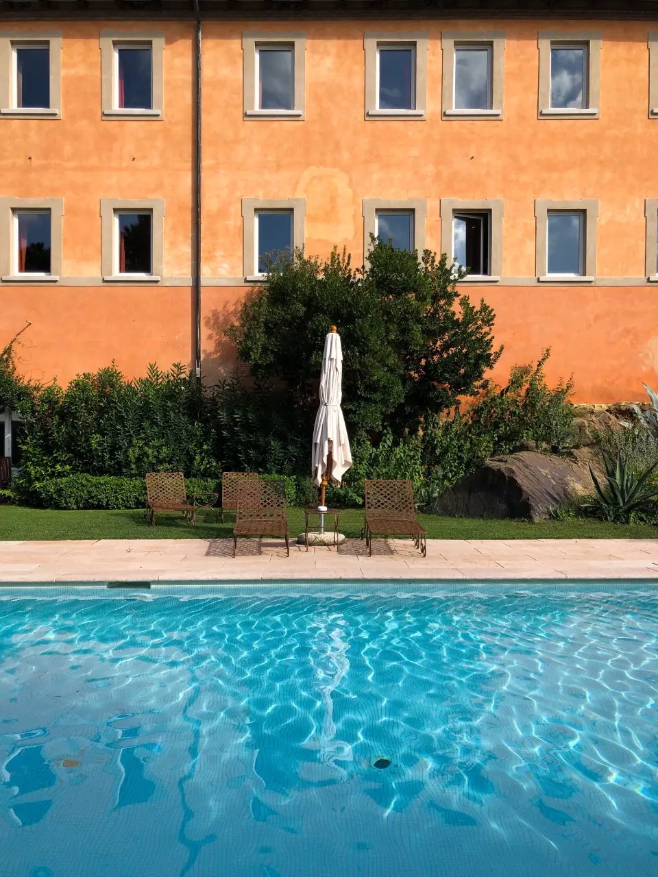 Piscina interrata davanti a una villa con facciata color arancio e giardino